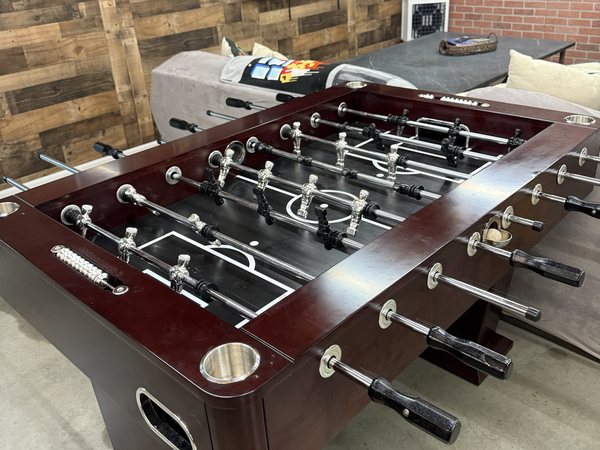 The foosball table with chrome players, in front of the wall and the sectional.