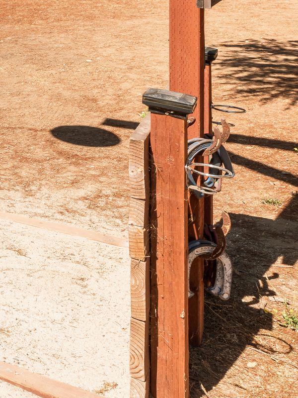 Horseshoes hanging on the post at the corner of the near pit, with the sand pit beside it.