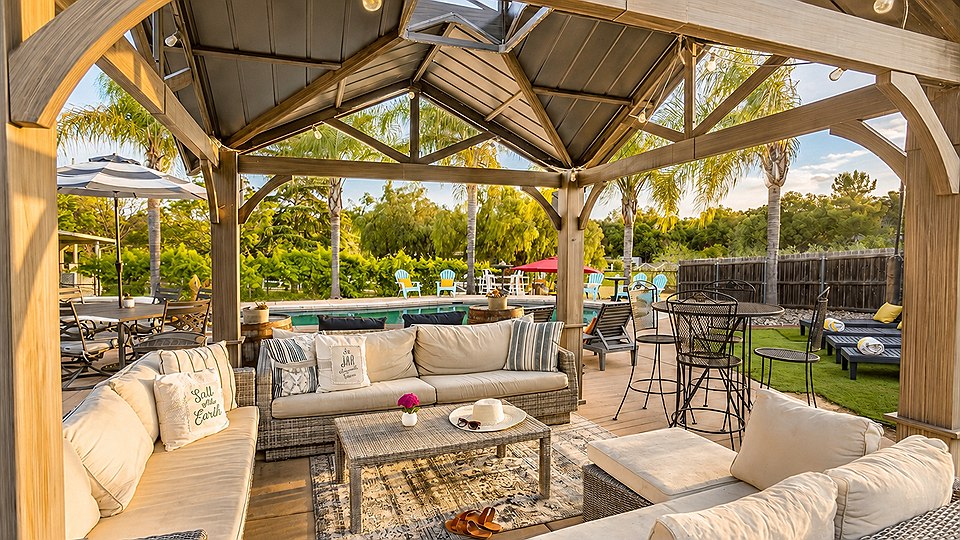 Cushioned outdoor sofas under a wooden pavilion, looking out across the pool deck.