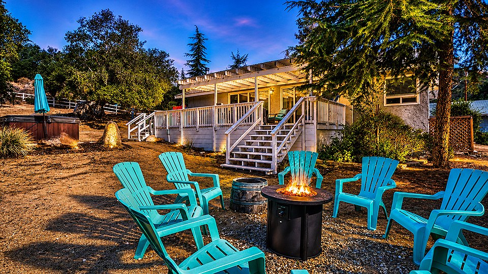 The fire pit lit at dusk at the foot of the deck, ringed by turquoise Adirondack chairs, with the hot tub off to one side.