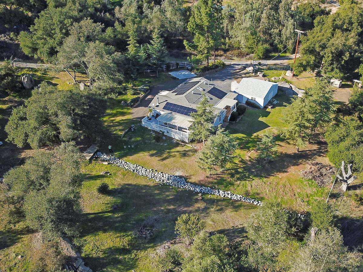 The property from the air: the house and deck surrounded by oak and pine, with a dry creek bed running through the meadow below.
