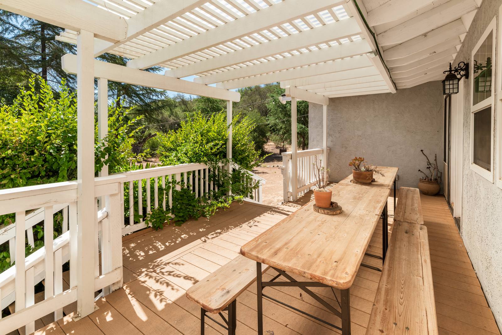 A long pine table with bench seating on the shaded end of the deck, under the pergola.