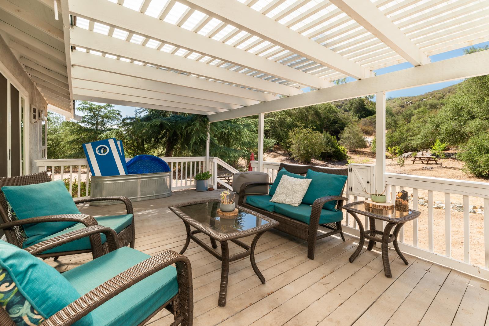The covered deck under a white pergola, with wicker seating, a stock-tank plunge pool and the hillside beyond.