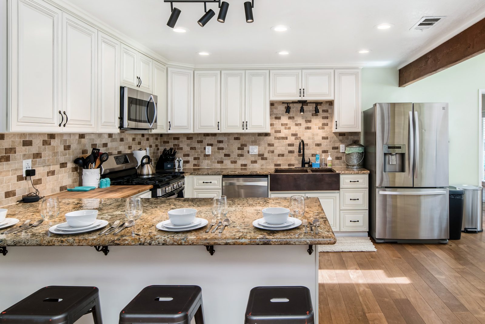 The kitchen with a gas range, a hammered copper farmhouse sink and a granite bar set for four.