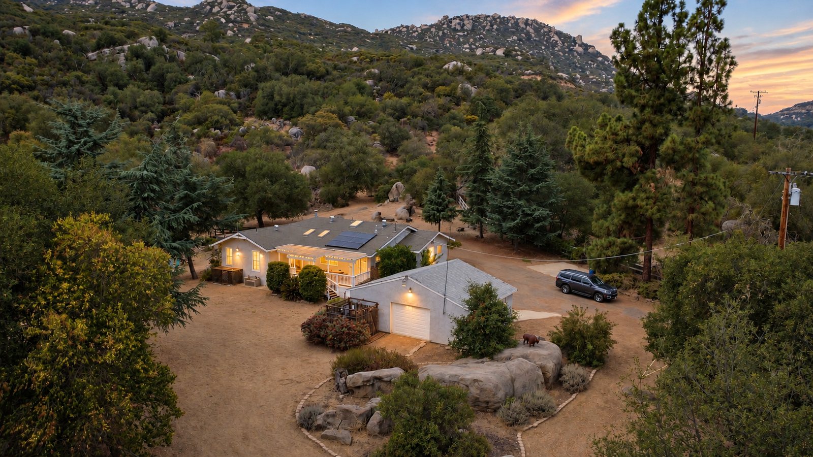 The house among tall pines at golden hour, with granite hills behind it.