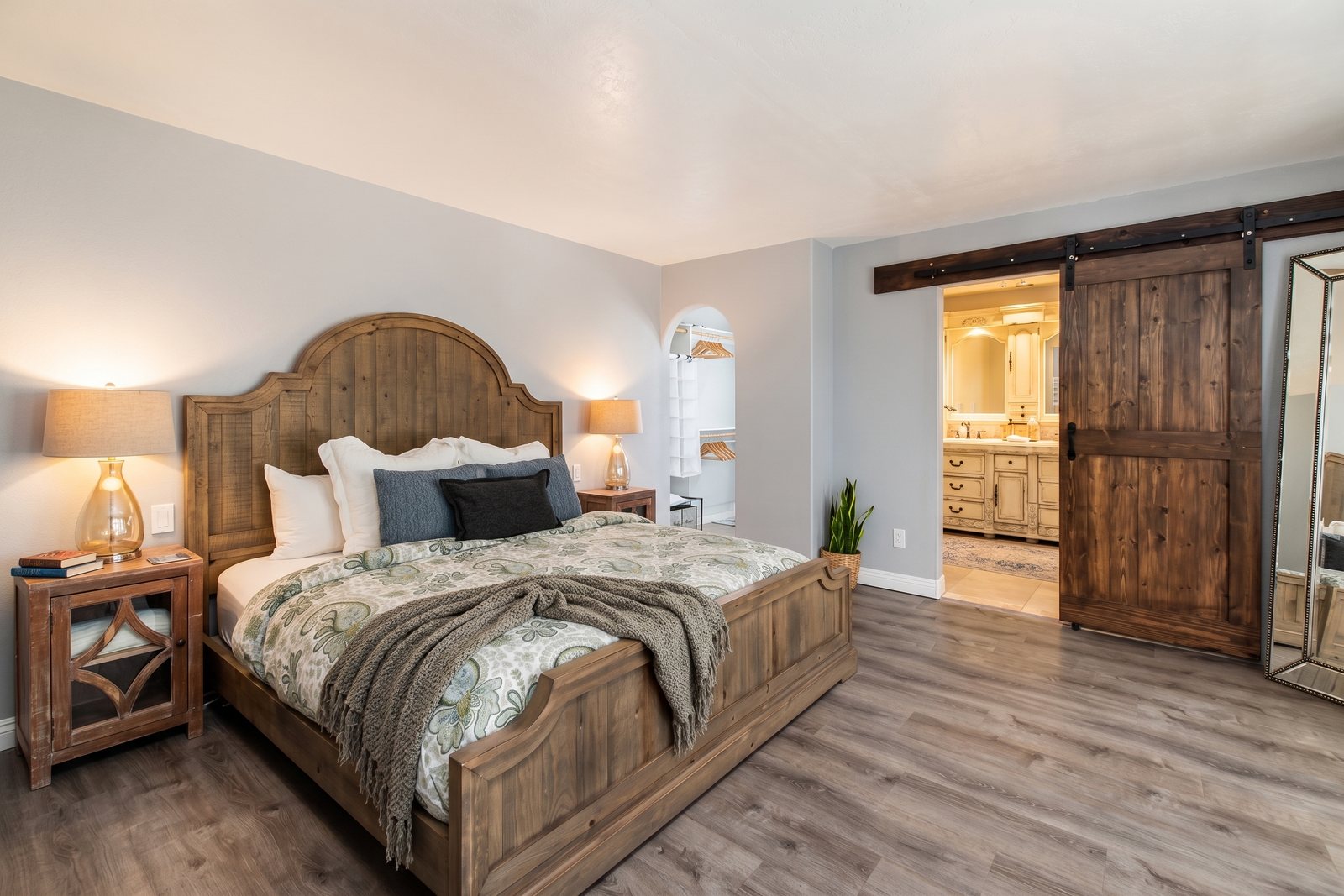 The primary bedroom: a king bed with a carved wood headboard, soft lamps and a sliding barn door.