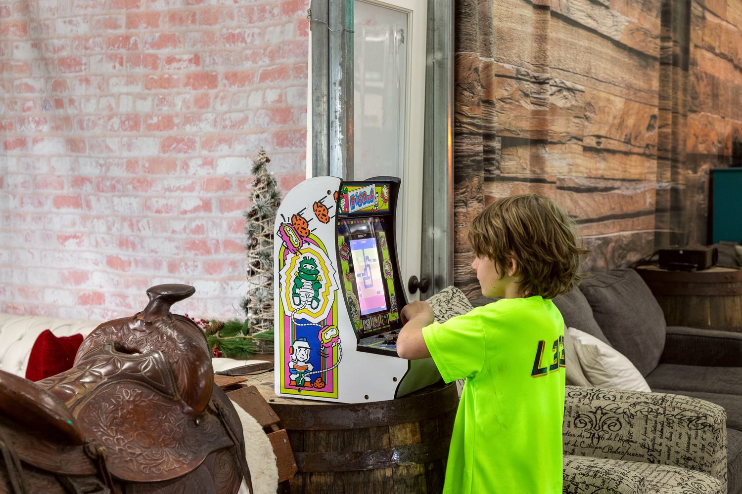 A boy playing a Dig Dug arcade cabinet set on a whiskey barrel.
