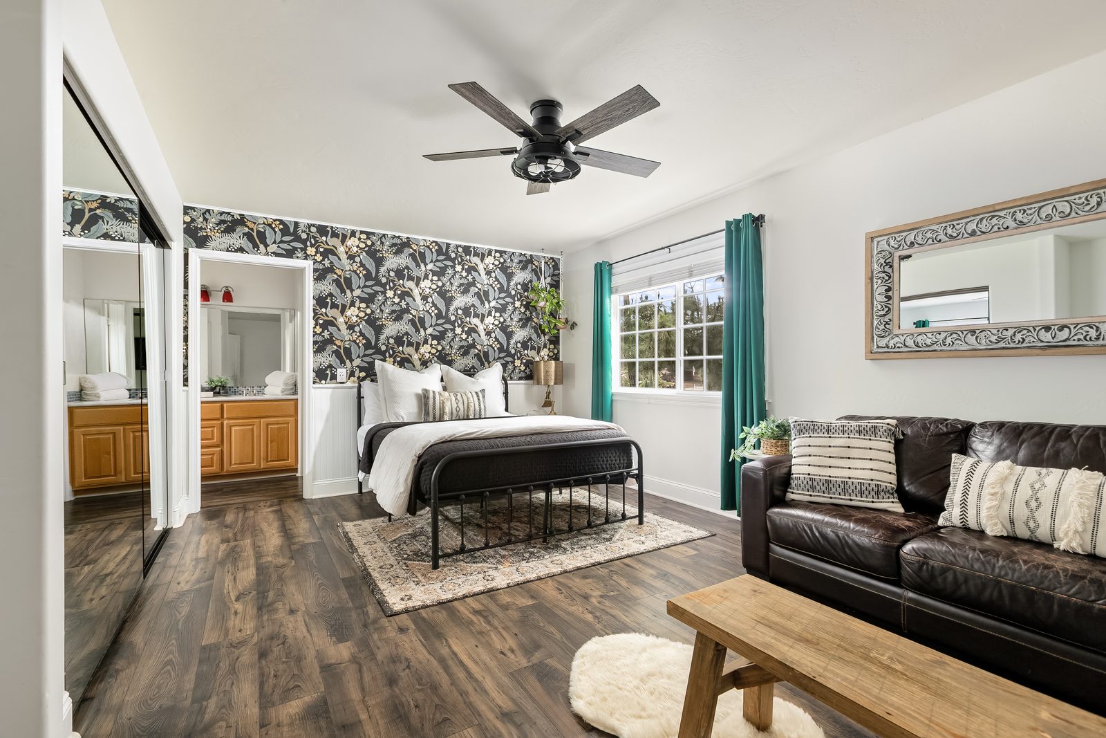 The Floral Peacock: a queen bed against dark botanical wallpaper, with a sitting area and a sleeper sofa.