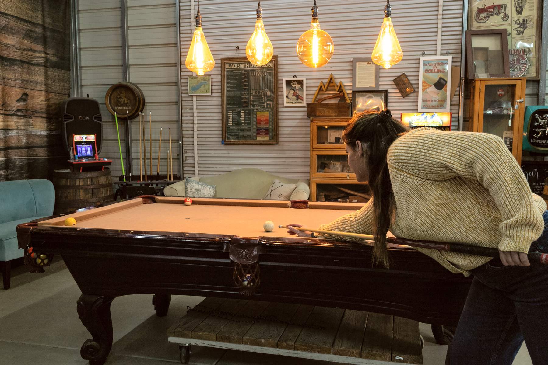 The barn game hall with a full-size pool table, arcade cabinets and oversized Edison bulbs overhead.