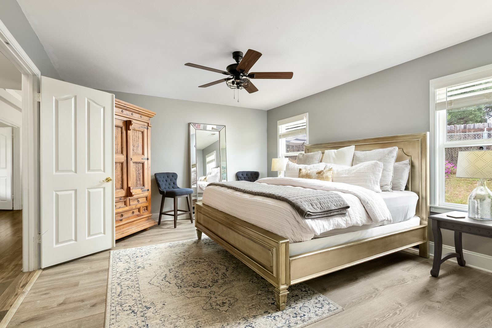 The Primary bedroom: a king bed with a carved armoire, a tall mirror and two velvet chairs by the window.