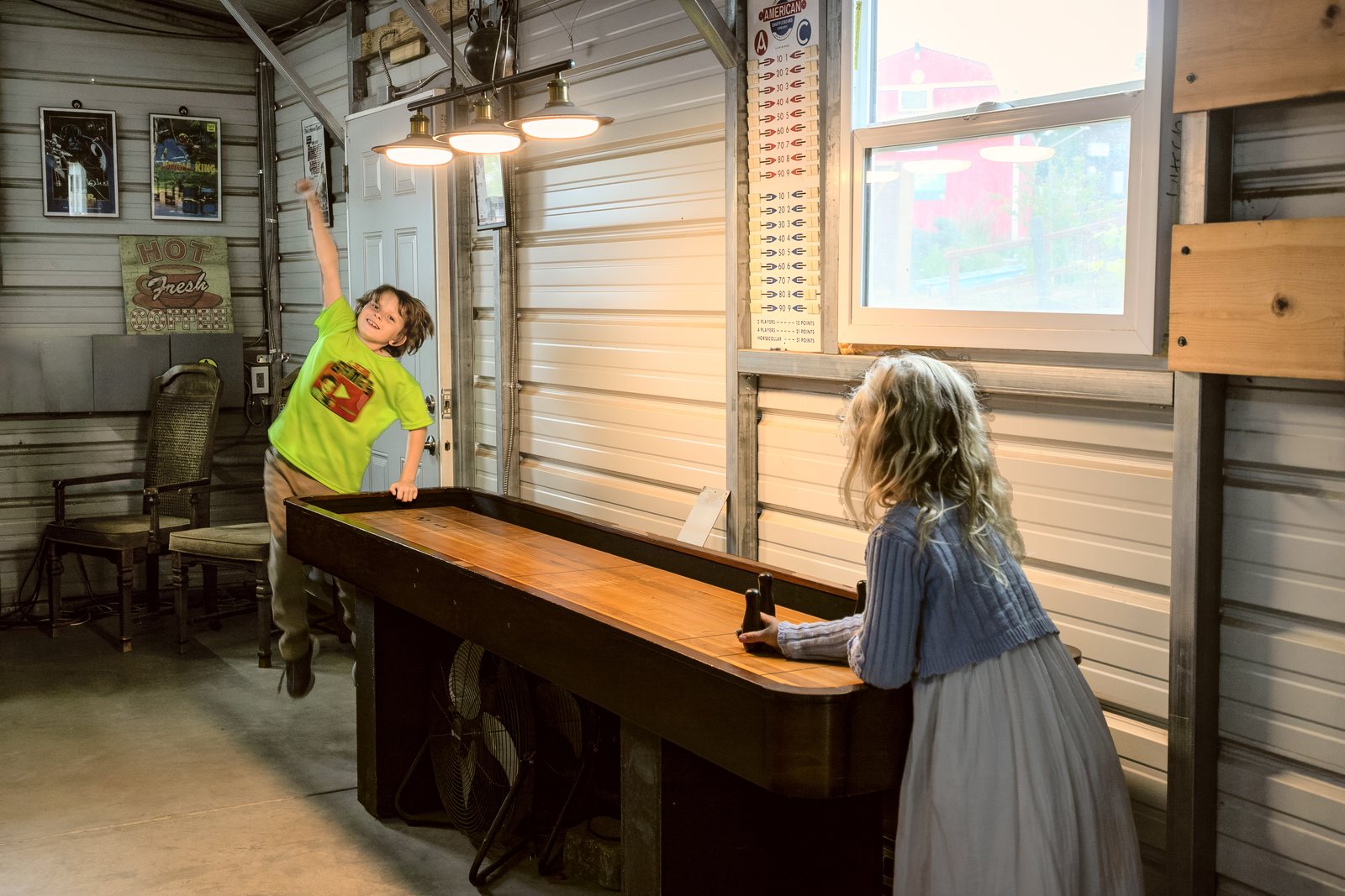 Two children playing shuffleboard in the barn, one throwing his arms up after a shot.