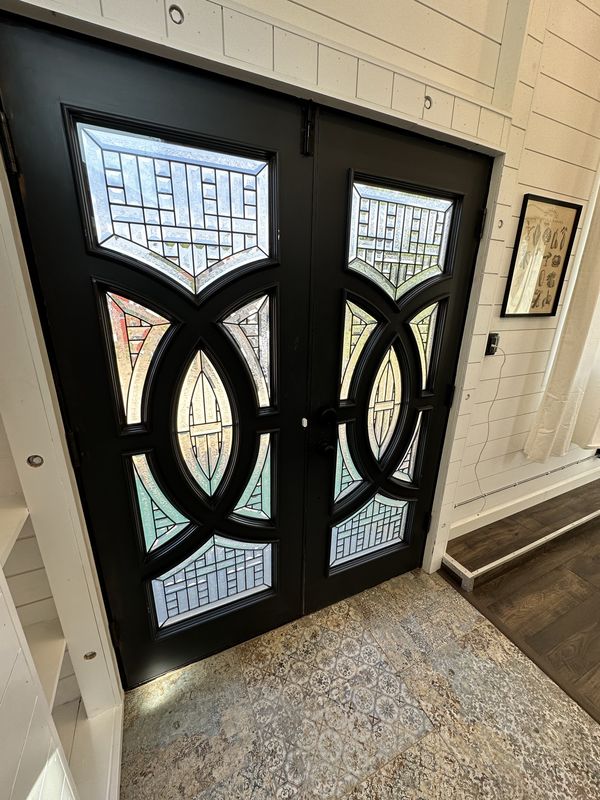 The black double doors from inside, with circular frames and colored leaded-glass panels.