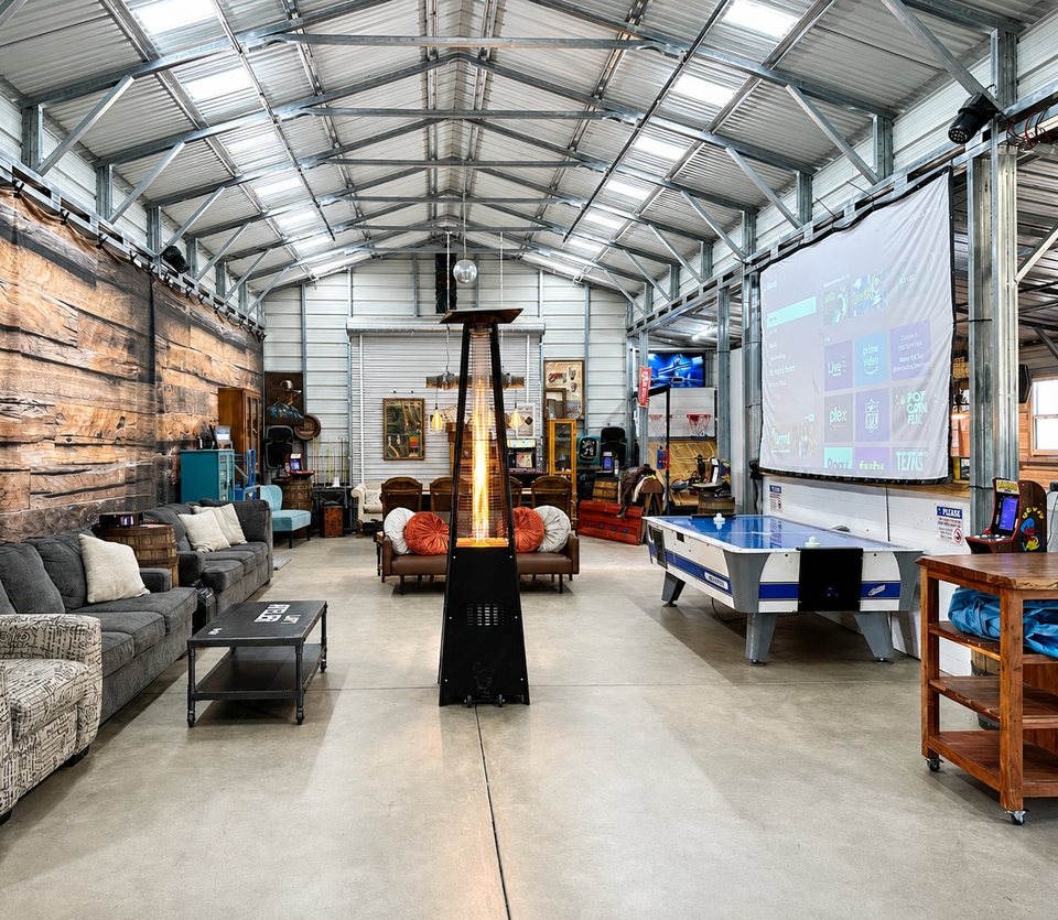 The barn hall with the sectional, a patio heater and the projection screen above the air hockey table.