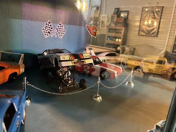 Die-cast cars on display behind glass, with checkered flags on the wall.
