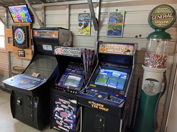 Arcade cabinets beside a gumball machine shaped like an old gas pump.