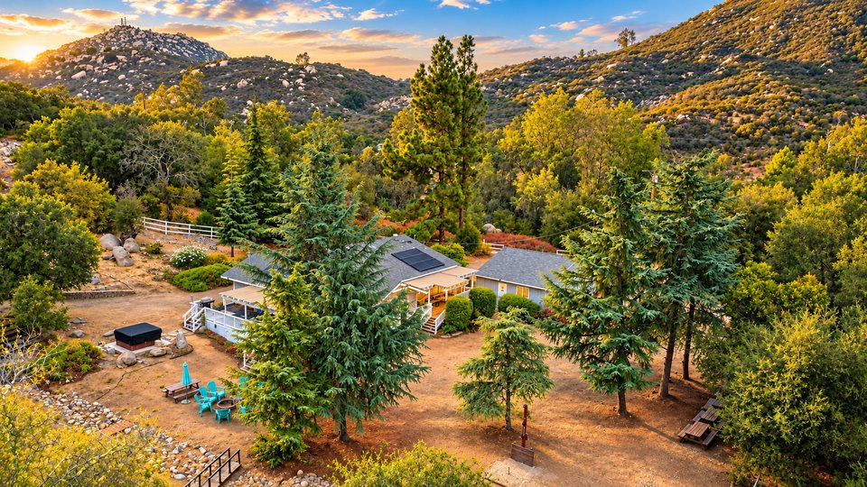 Mountain Retreat from the air at golden hour: the house, deck and hot tub among the pines, with the granite summit of Mount Woodson behind.